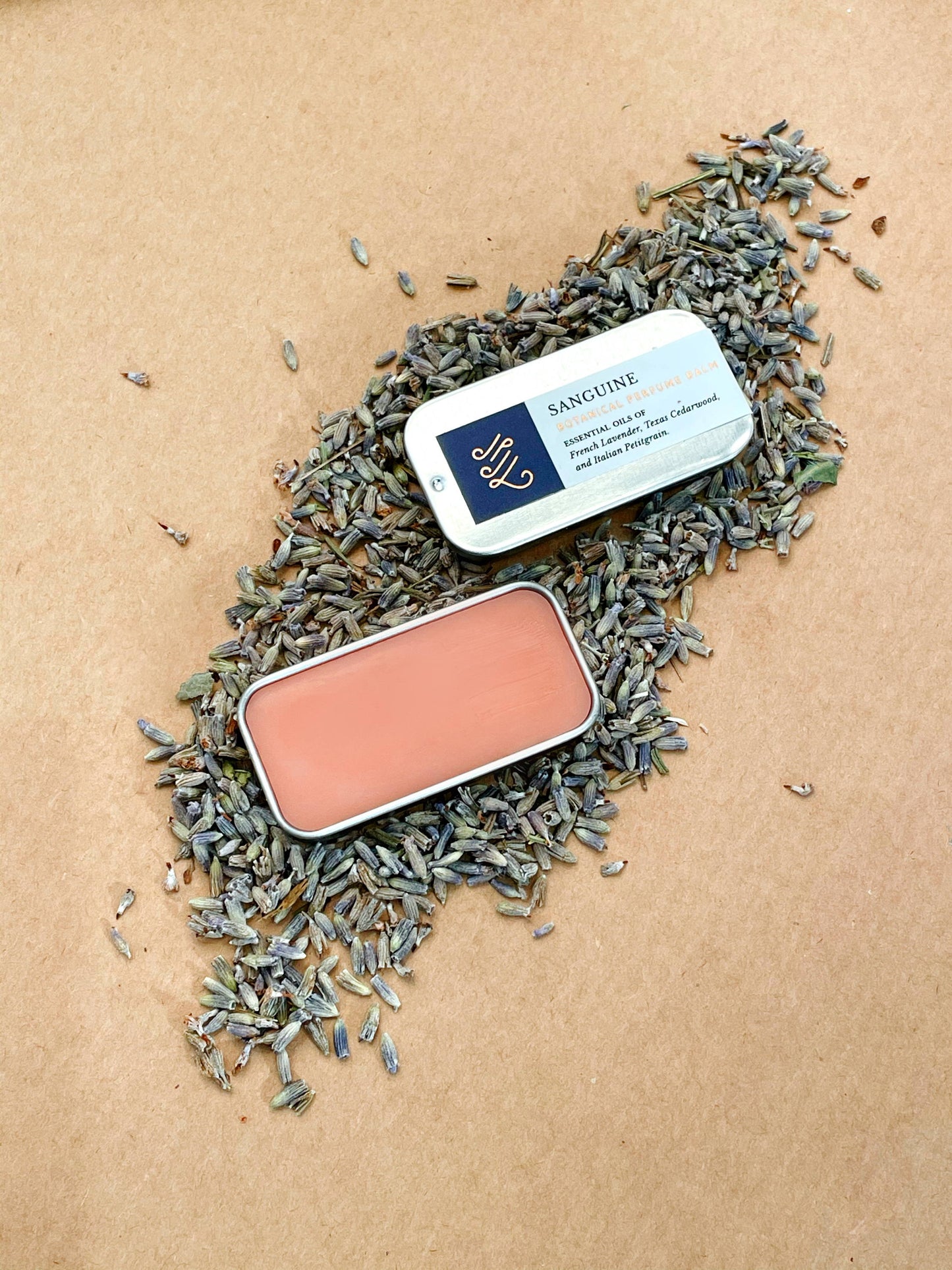 A natural perfume balm in a tin sitting on dried lavender handmade by Even keel, with the lid open showing the pink color of the balm.
