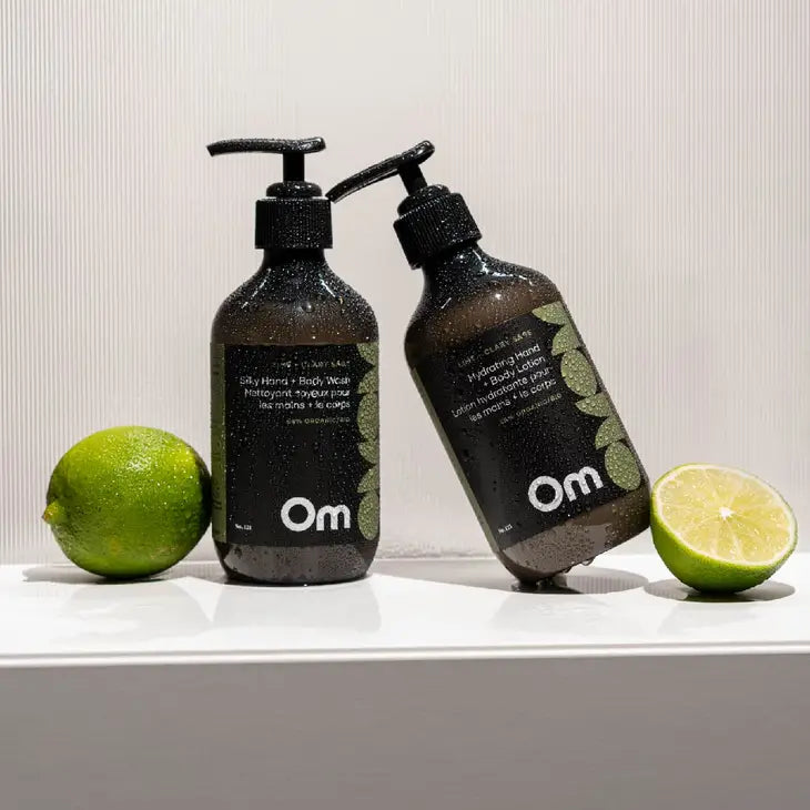 A natural hand and body wash bottle and a matching hand and body lotion from Om Organics with two limes on either side in a shower.