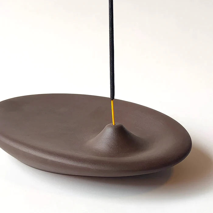 An incense holder in dark brown color, handmade with ceramic stoneware by Siesta Studio, Turkey, holding an incense stick.