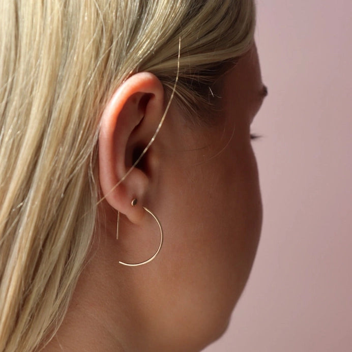 A curved earring in 14k yellow gold fill that threads through the ear piercing, by Token Jewelry.