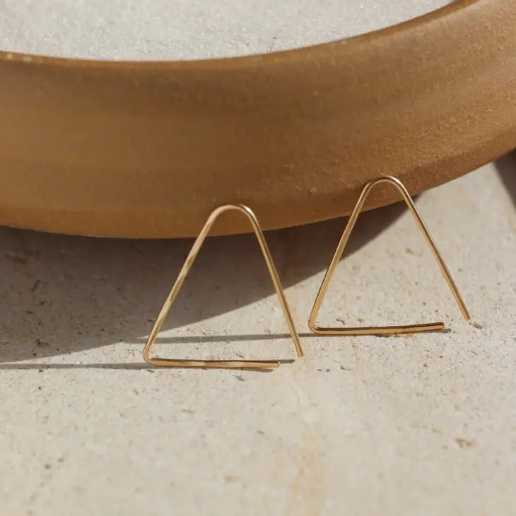 A triangle shaped earring in 14k yellow gold fill that threads through the ear piercing, by Token Jewelry.