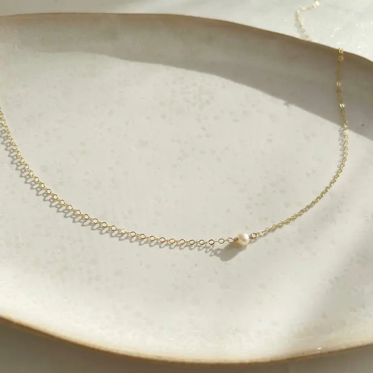 A gold-filled necklace with mini pearl laying flat on a plate, by Token Jewelry.