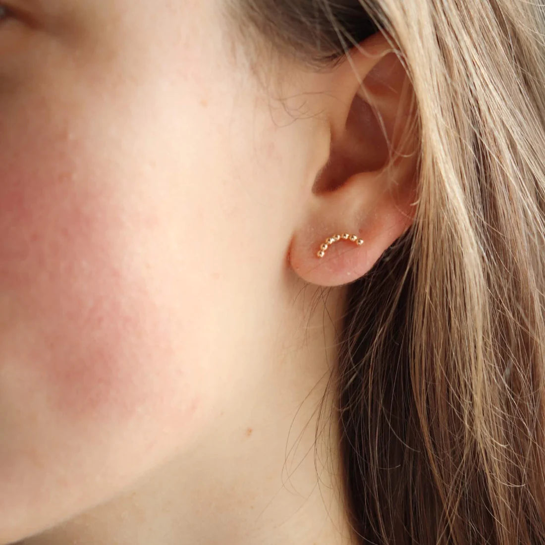 Close up of someone wearing an arched stud earring in 14k yellow gold fill, by Token Jewelry.