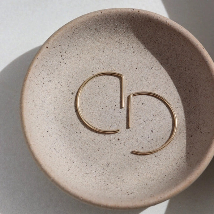 A curved earring in 14k yellow gold fill that threads through the ear piercing laying flat on a plate, by Token Jewelry.
