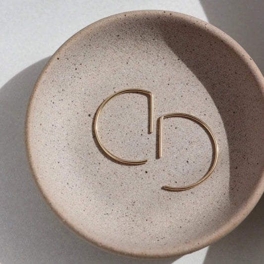 A curved earring in 14k yellow gold fill that threads through the ear piercing laying flat on a plate, by Token Jewelry.
