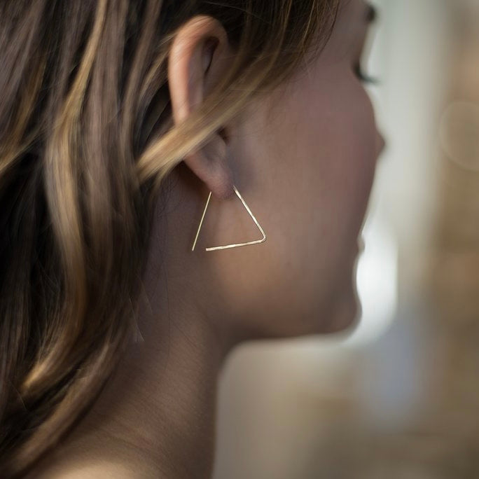 A gold-filled earring in shape of a triangle that threads through the ear piercing.